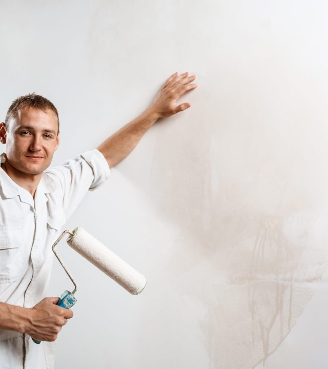 Professional worker looking at camera, holding roller over white wall. Copy space.